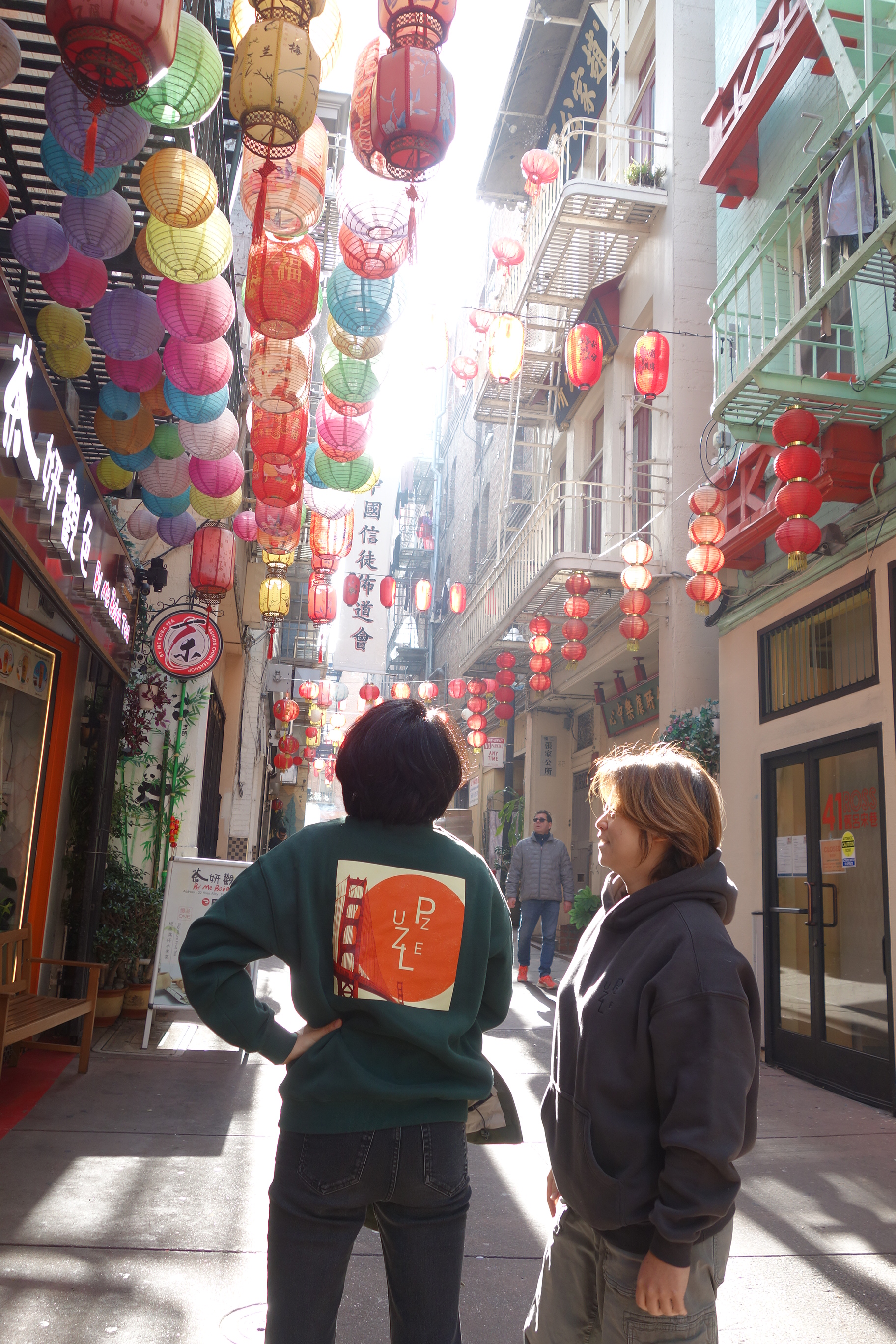 Two people beneath colorful lanterns in San Francisco’s Chinatown, one wearing a Puzzle sweatshirt