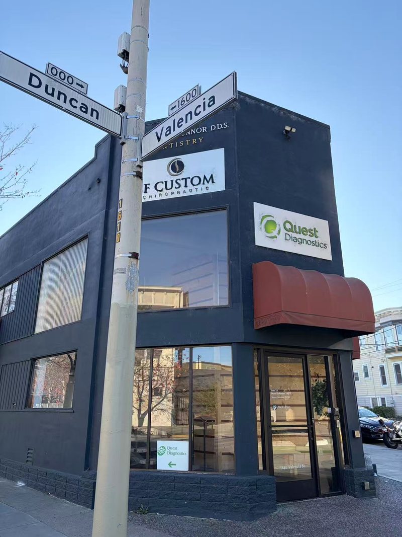 The corner of Valencia and Duncan: a dark gray building with a Quest Diagnostics sign and a red awning over a glass front door.