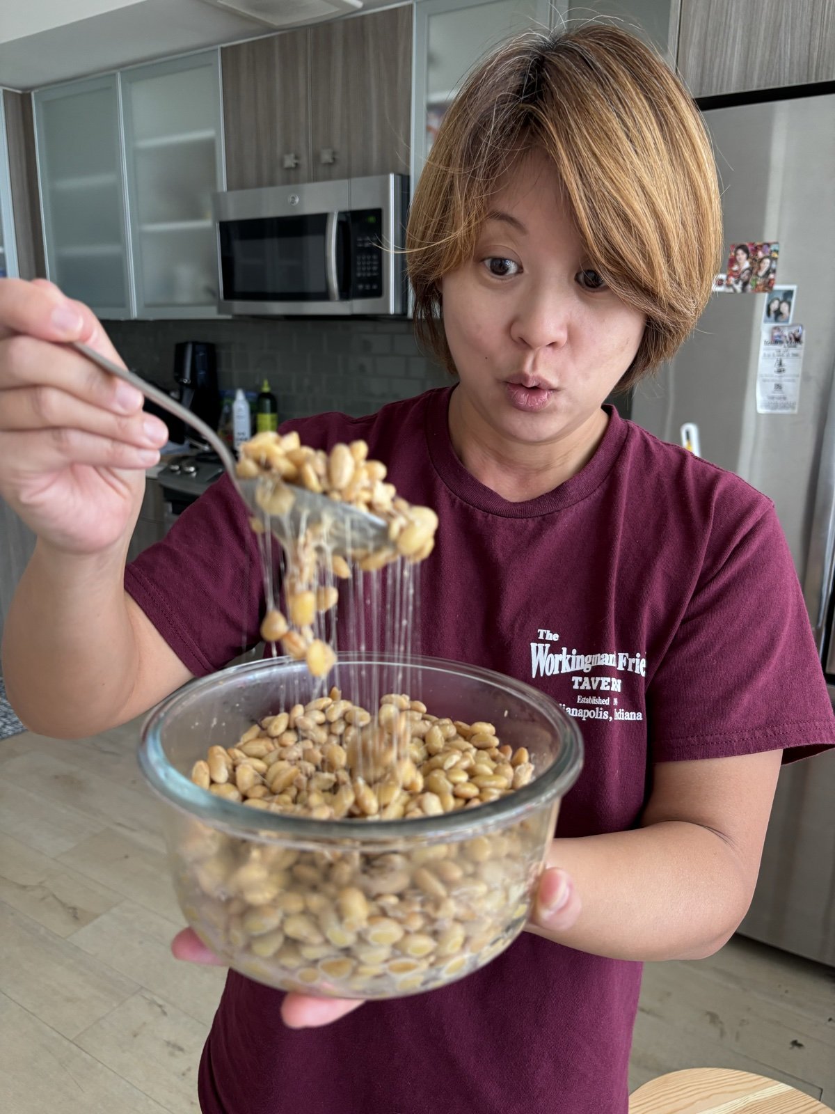 Dr Deb Ma in her kitchen, lifting a forkful of natto out of a glass bowl and watching the strands pull.