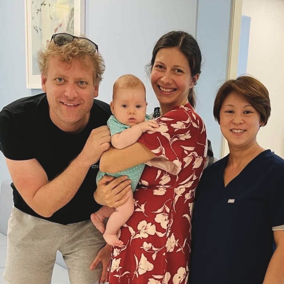 A smiling couple holding their baby, with Dr. Deb at the clinic
